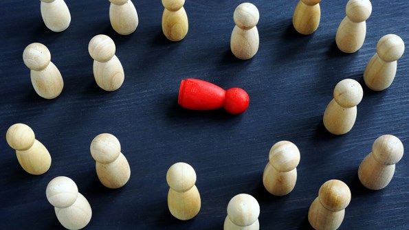 white figurines meant to symbolize humans surround a red figurine on a black surface. the red figurine is prone on the ground