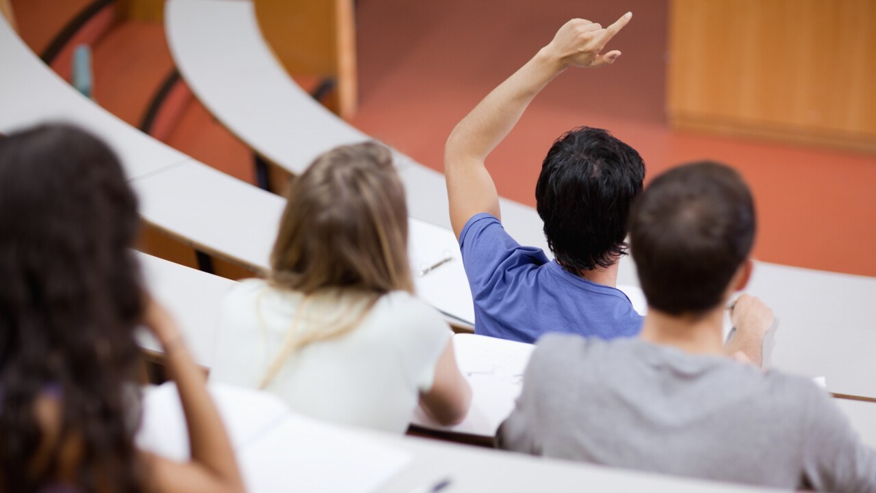 A student in a lecture hall has his hand raised.