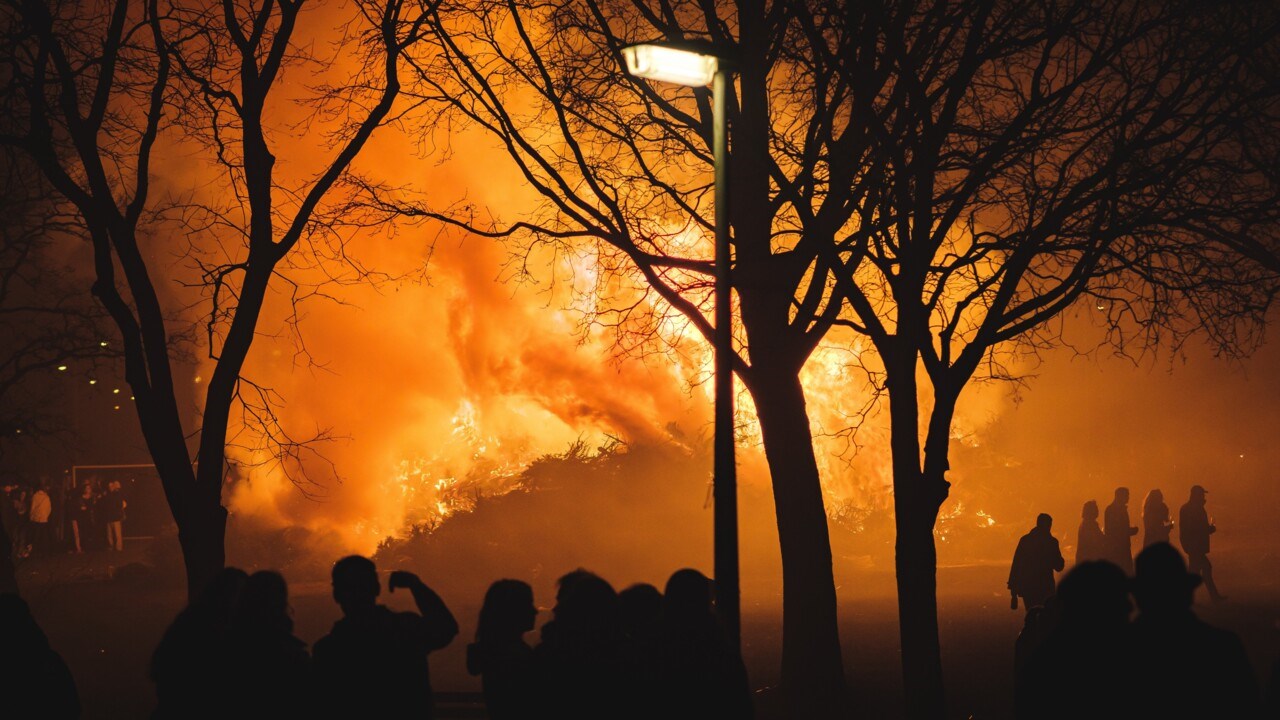 Flammor från intensiv skogsbrand med mänskliga silhuetter i förgrunden