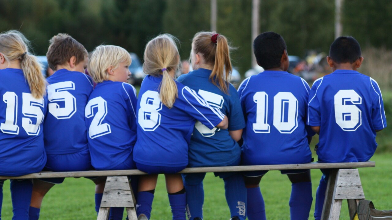 Barn i fotbollskläder sitter på en bänk.