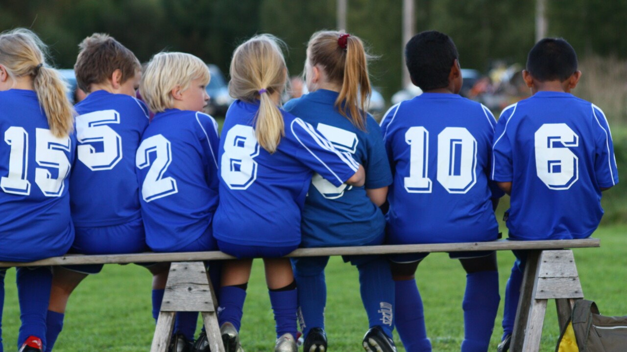 Barn i fotbollskläder sitter på en bänk.