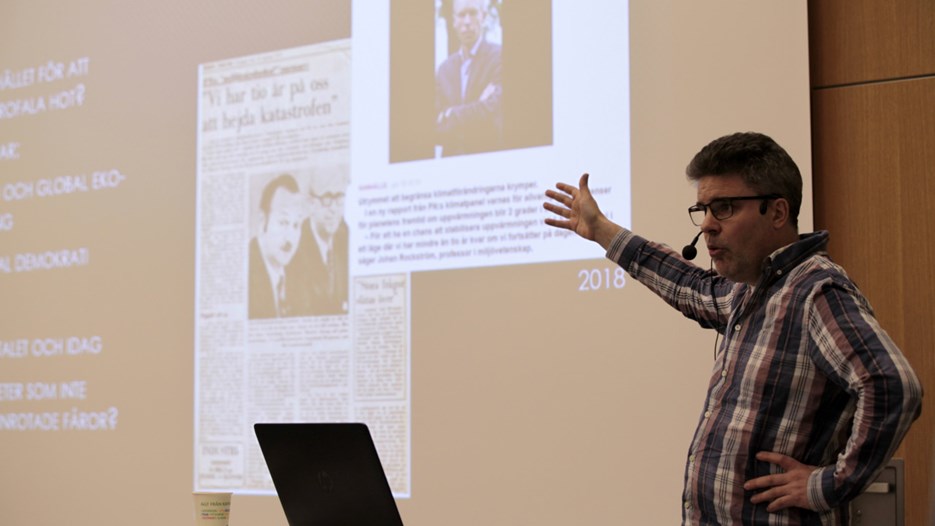 En man gestikulerar framför en skärm som visar en powerpointpresentation vid en föreläsning vid Umeåuniversitet.