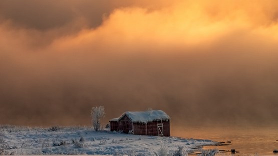 Snowed over barn by the riverside.
