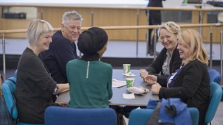 En grupp människor möts, samtalar och skrattar runt ett bord på Umeå universitet. 