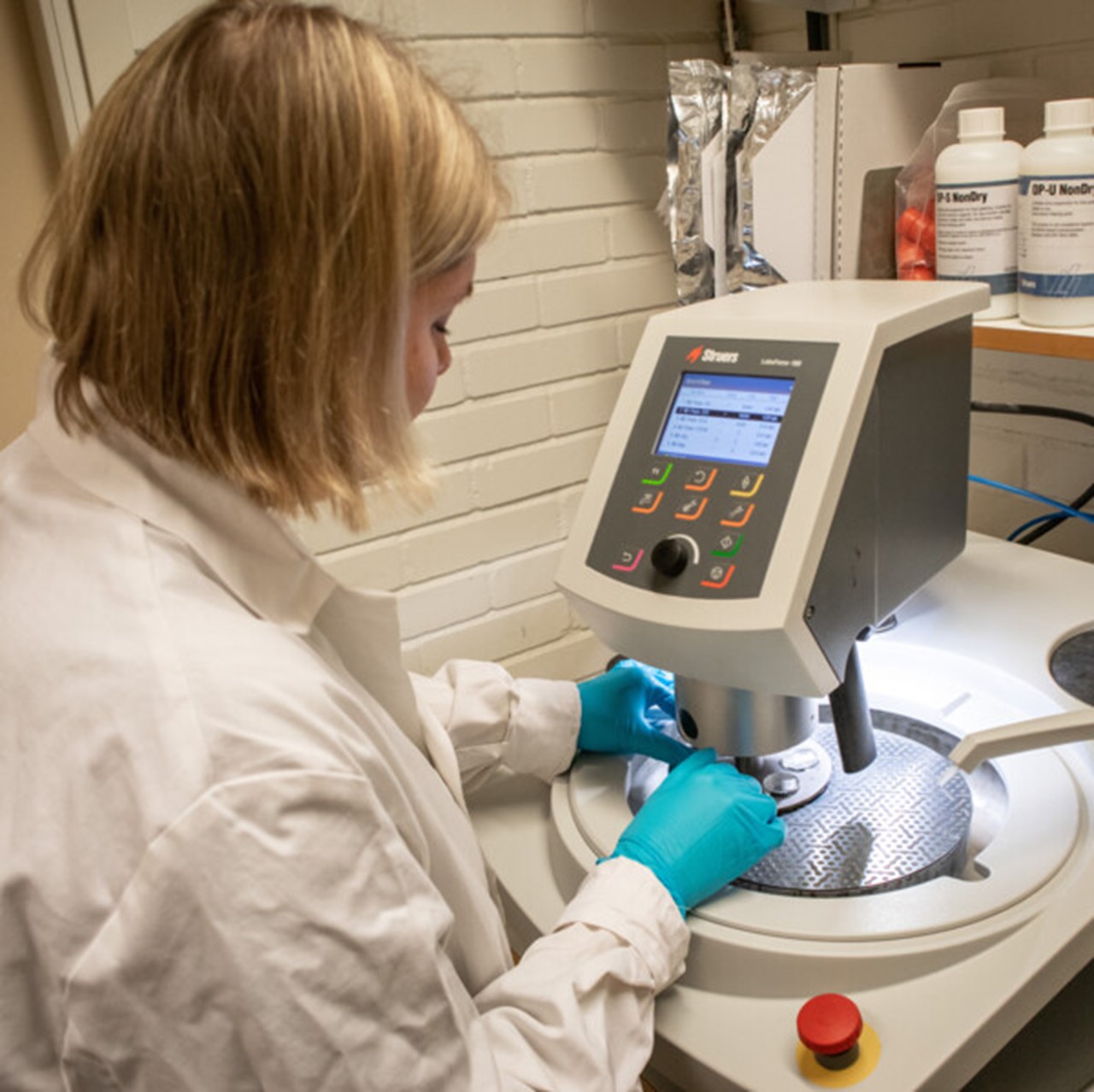 Kvinna i vit labbrock och handskar i ett laboratorium.
