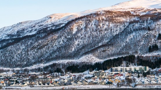 Småstaden Tromsö, syns i en backe nedanför en fjällrygg.