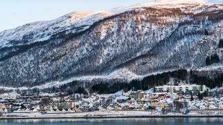 The small Norwegian city Tromsö, seen from below a snowy mountainside.