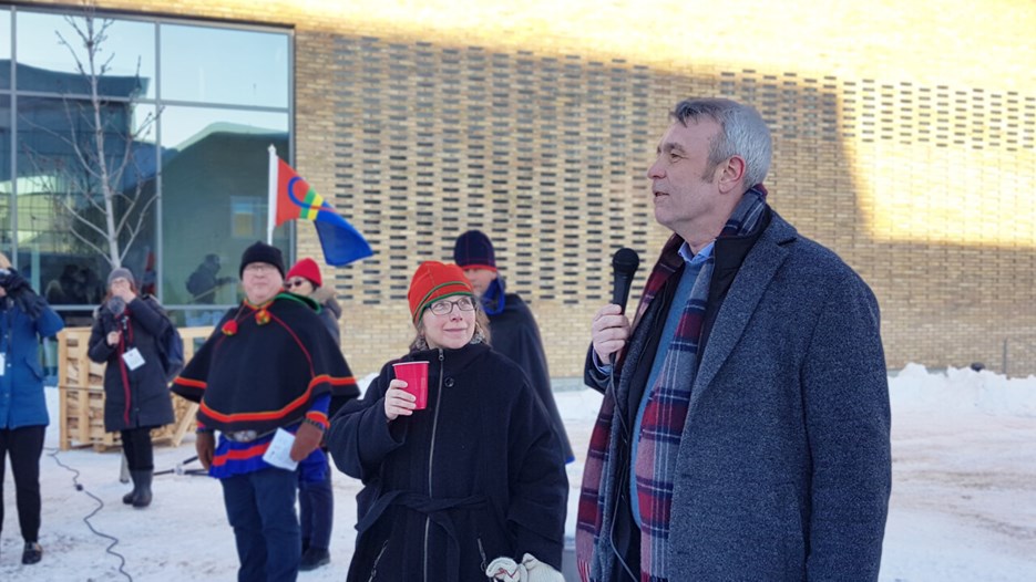 Peter Sköld och Lena Maria Nilsson står framför publik utanför humanisthuset, med en samisk flagga vajandes i bakgrunden.
