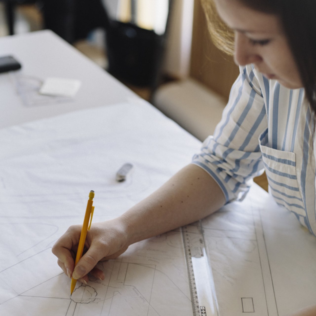 Student på Arkitekthögskolan skissar vid sitt skrivbord.