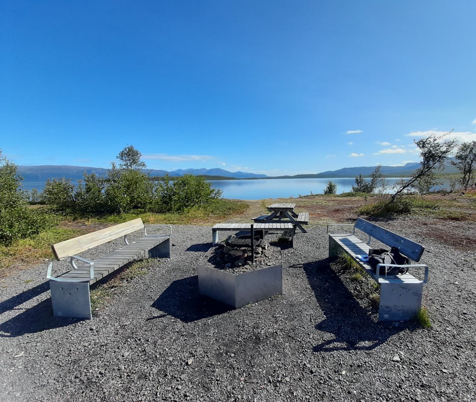 A fire place near a lake in Abisko, with a blue sky and mountains in the distance