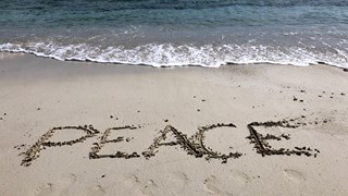 Strand med havet i bakgrunden. I sanden står texten Peace. 
