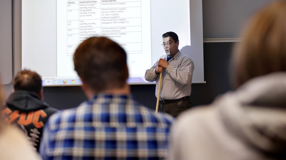 Läraren Johan Hansson undervisar en grupp studenter i en lektionssal på campus.
