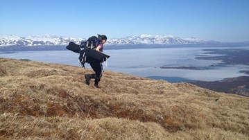 En forskare som bär på utrustning i sjö- och fjällmiljö.