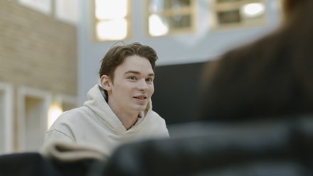 Studenter sitter och pluggar vid ett runt bord i ett bibliotek. 