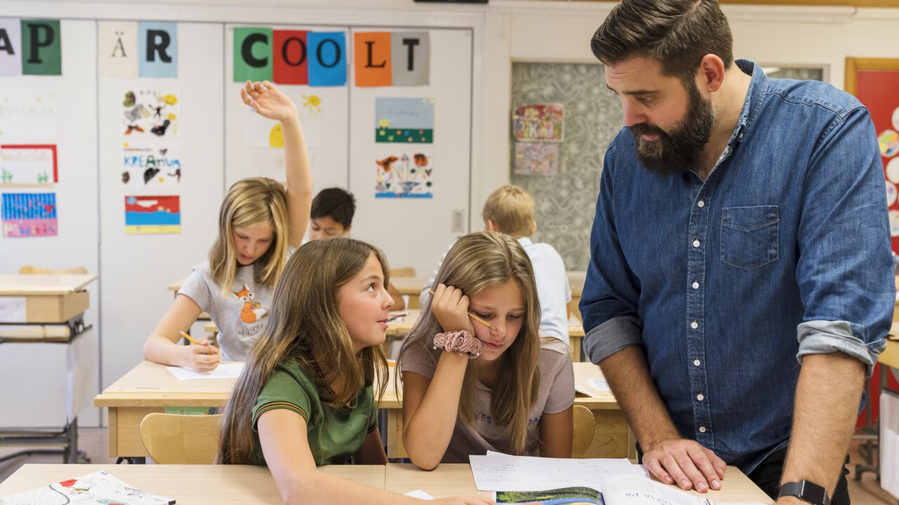 En lärare hjälper två elever i skolmiljö.