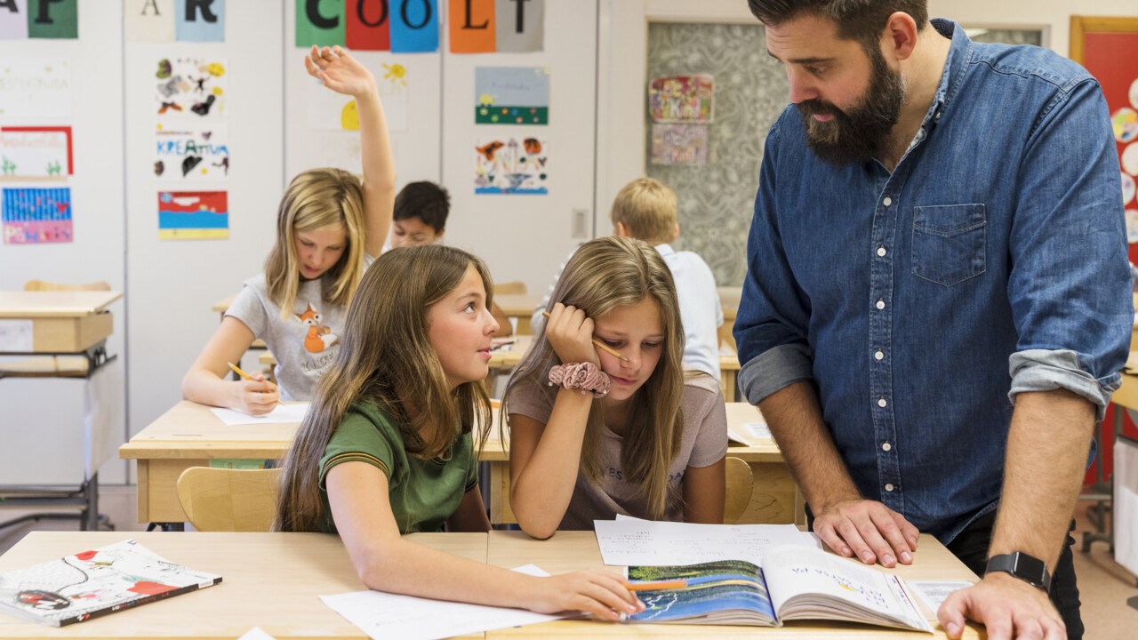 En lärare hjälper två elever i skolmiljö.