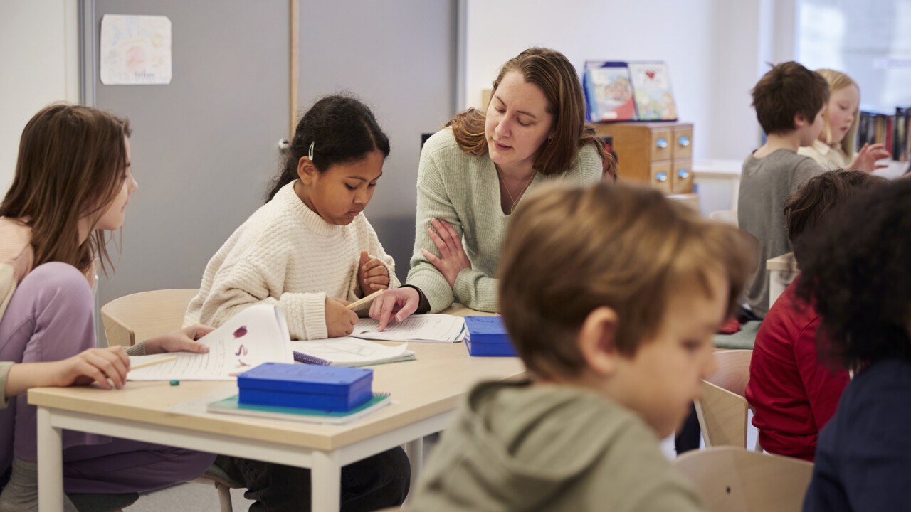 Teacher helping children with a task, in a classroom.