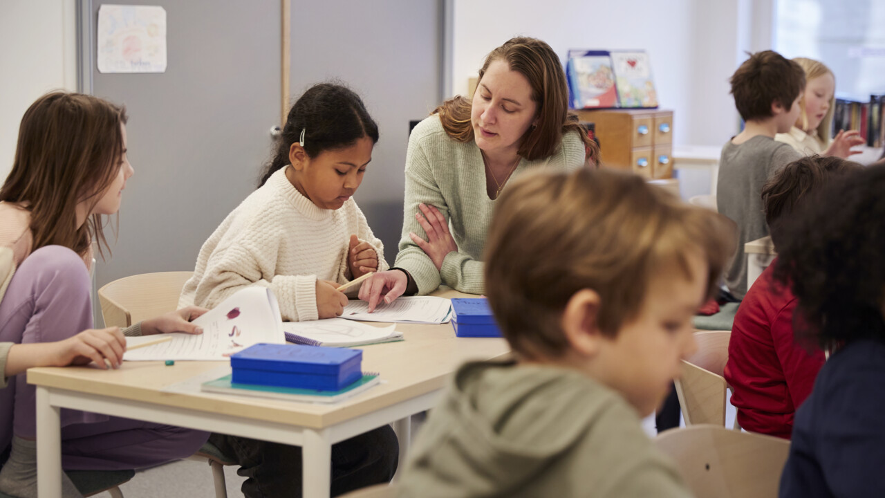 Lärare hjälper barn med uppgift, i klassrum.