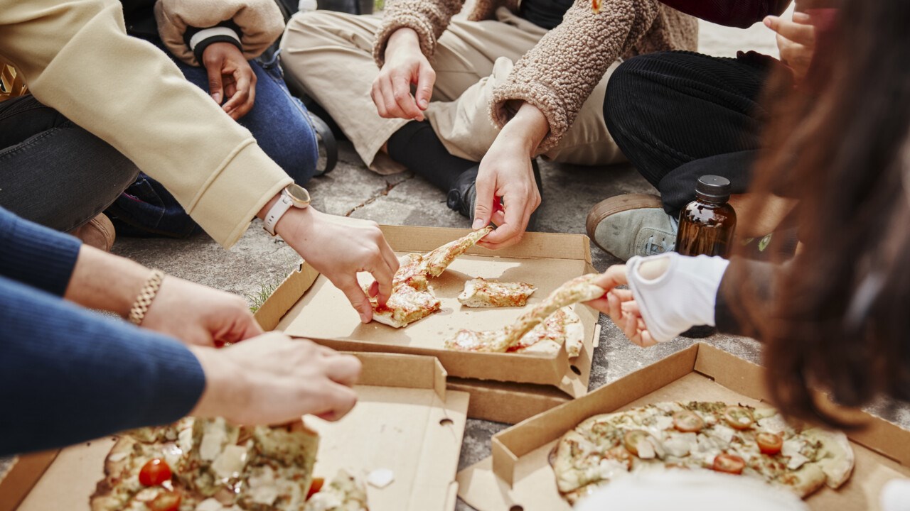 Närbild på händer som sträcker sig efter pizza.