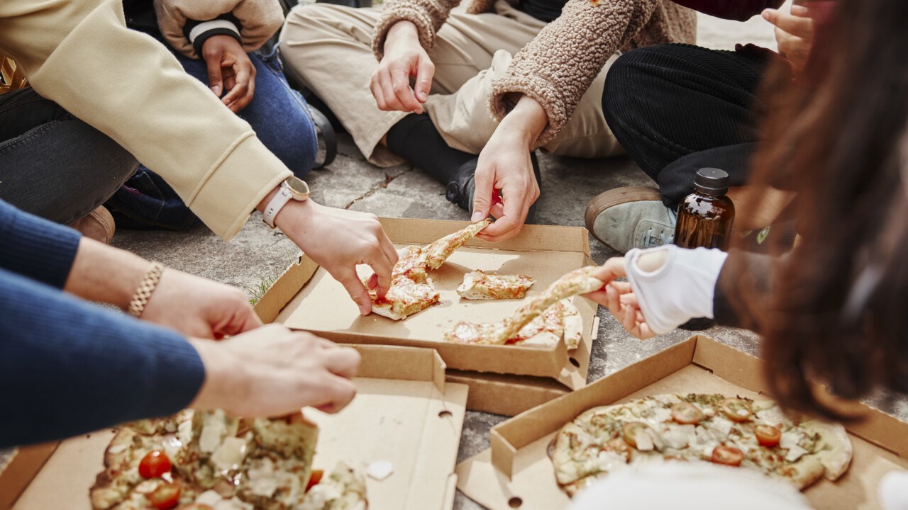 Närbild på händer som sträcker sig efter pizza.