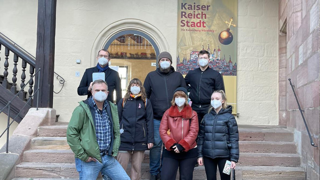 Sju personer iförda munskydd står på en trappa till en byggnad och tittar mot fotografen
