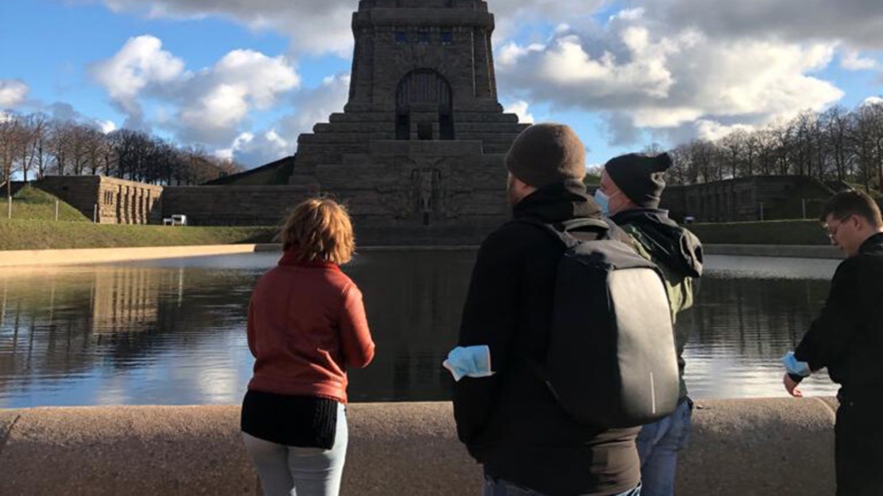 Fyra studenter vända bort från fotografen står på en stenbro och beskådar ett stenmonument i vattnet.