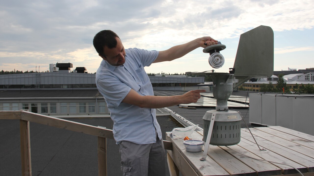 Foto av en man som står på ett tak och håller i en liten metalltrumma framför ett större föremål i metall