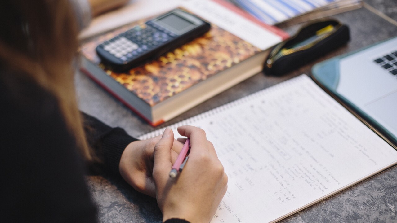 Photo of a student holding a pen in front of books