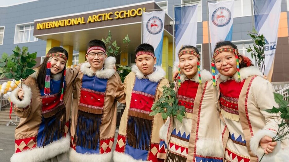 Five students from the school dressed in traditional clothes smiling in front of the entrance