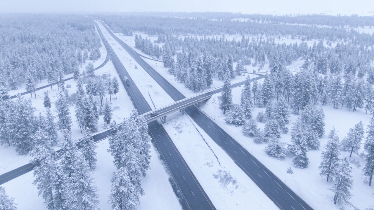 Ett vinterlandskap där man ser vägar och en bro i fågelperspektiv med snöiga granar.