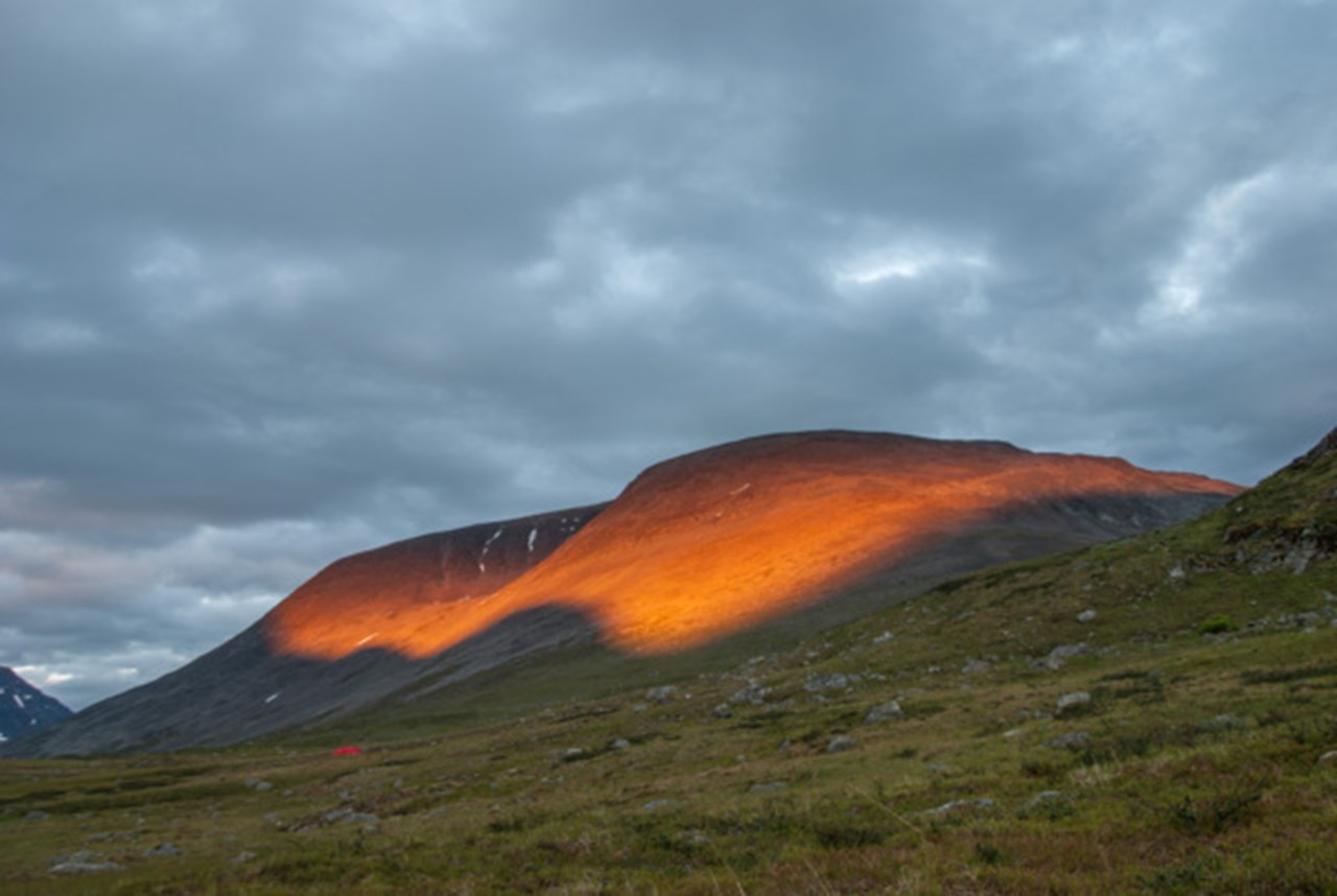 Solen lyser på ett berg i svenska fjällen.