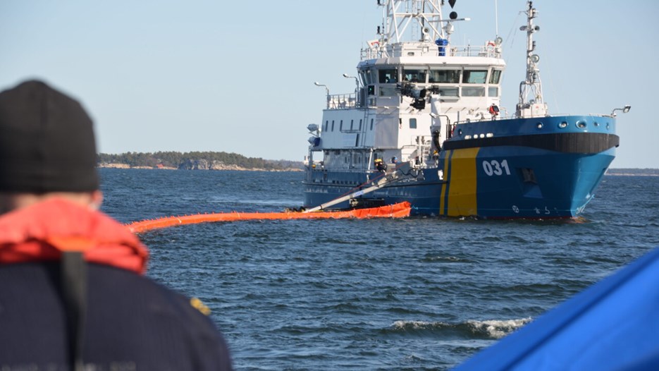 Ett kustbevakningsfartyg samlar upp olja från vatten.