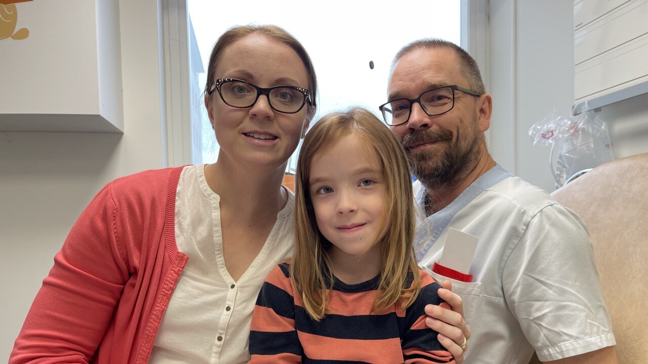 Gruppbild inomhus med Alma mellan mamma och pappa.