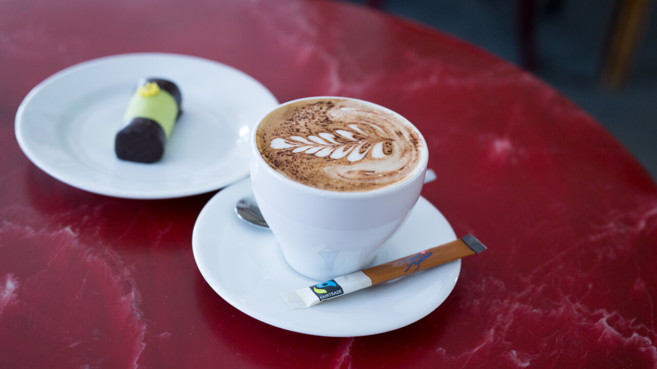 Närbild på kopp med cappuciono-kaffe och dammsugare.