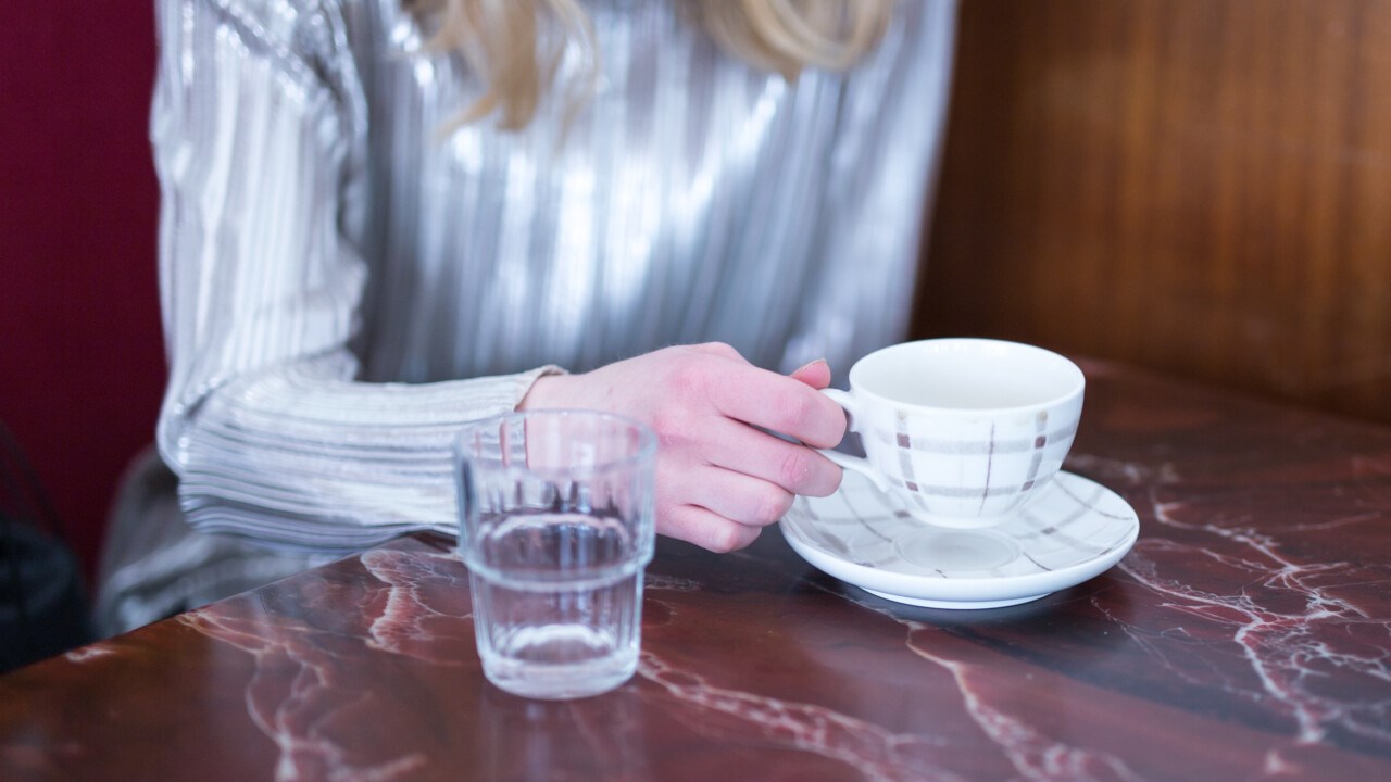 Detalj på person med kaffekopp på ett café.
