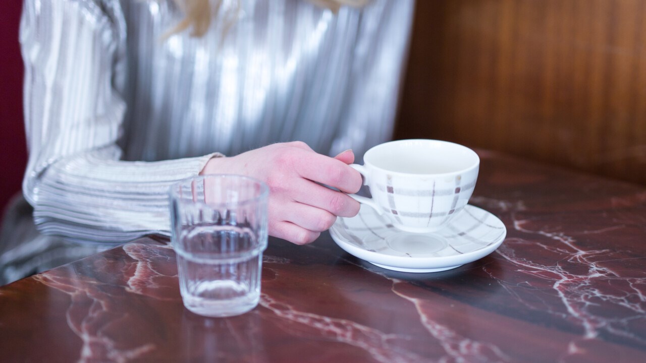 Detalj på person med kaffekopp på ett café.