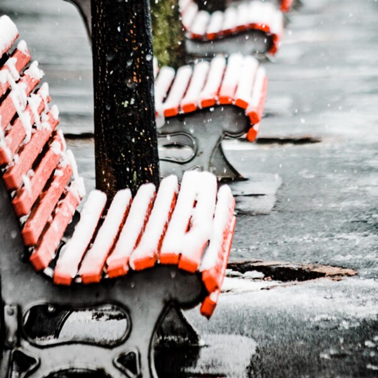 En länga med röda träbänkar täckta med snö på en isig gata.