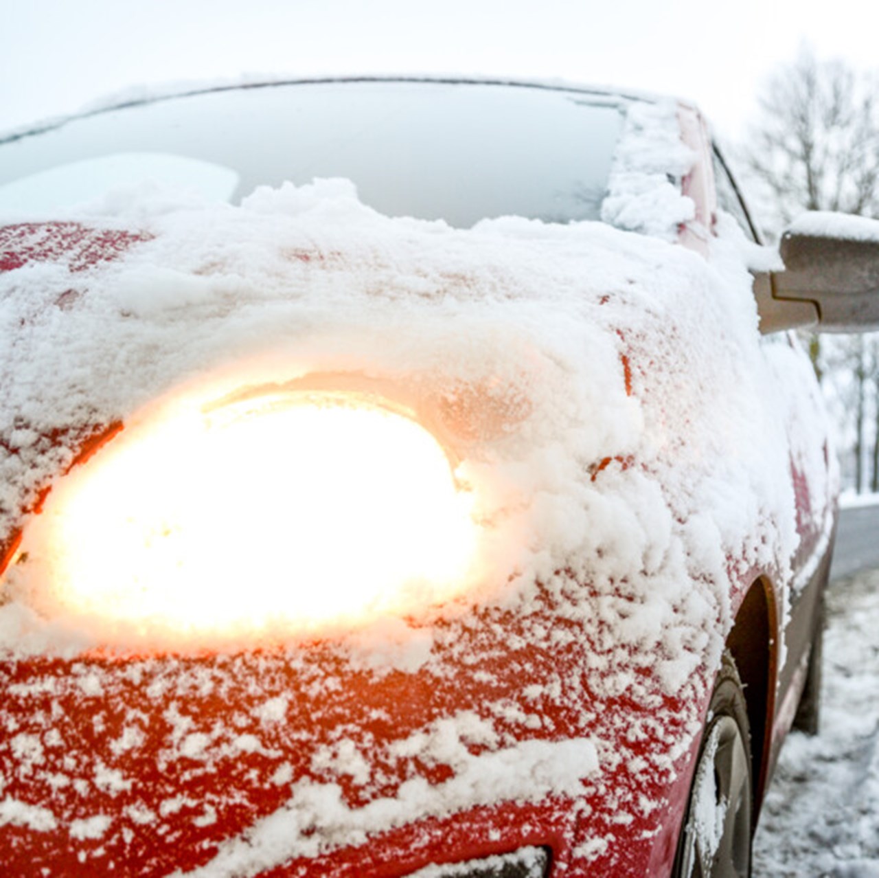 Strålkastaren är påslagen och skiner genom isen på en snöbetäckt röd bil