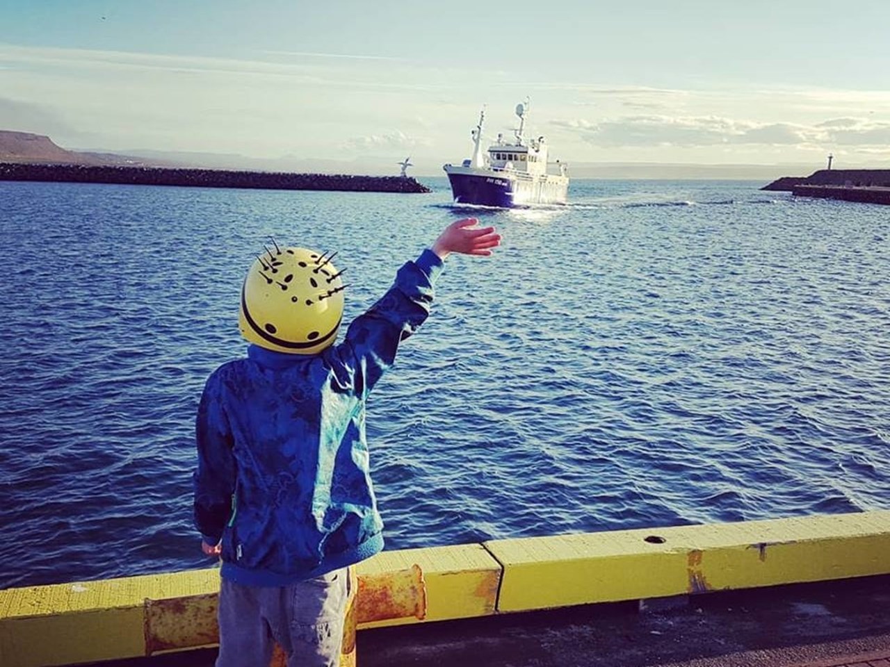 En pojke vinkar till en fikskebåt
