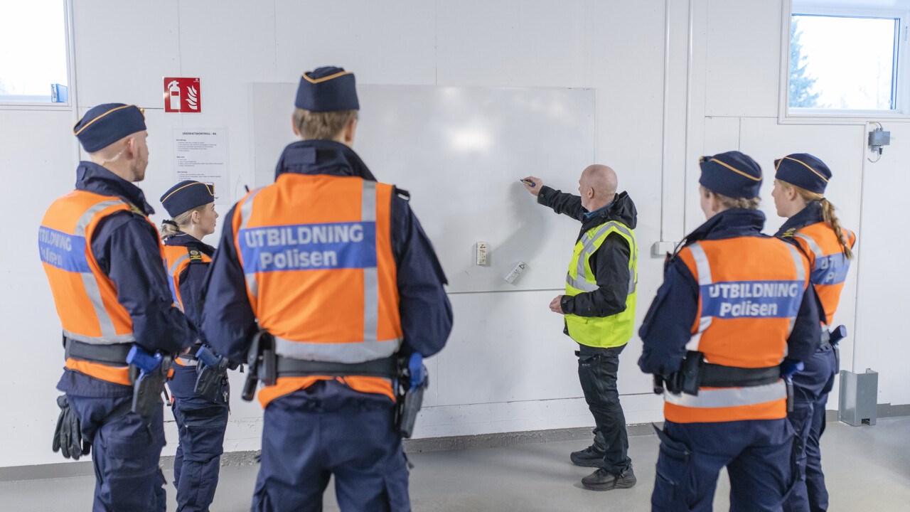 Polislärare Conny Tärnklev instruerar polisstudenter vid vita tavlan i Polisutbildningshusets garage.