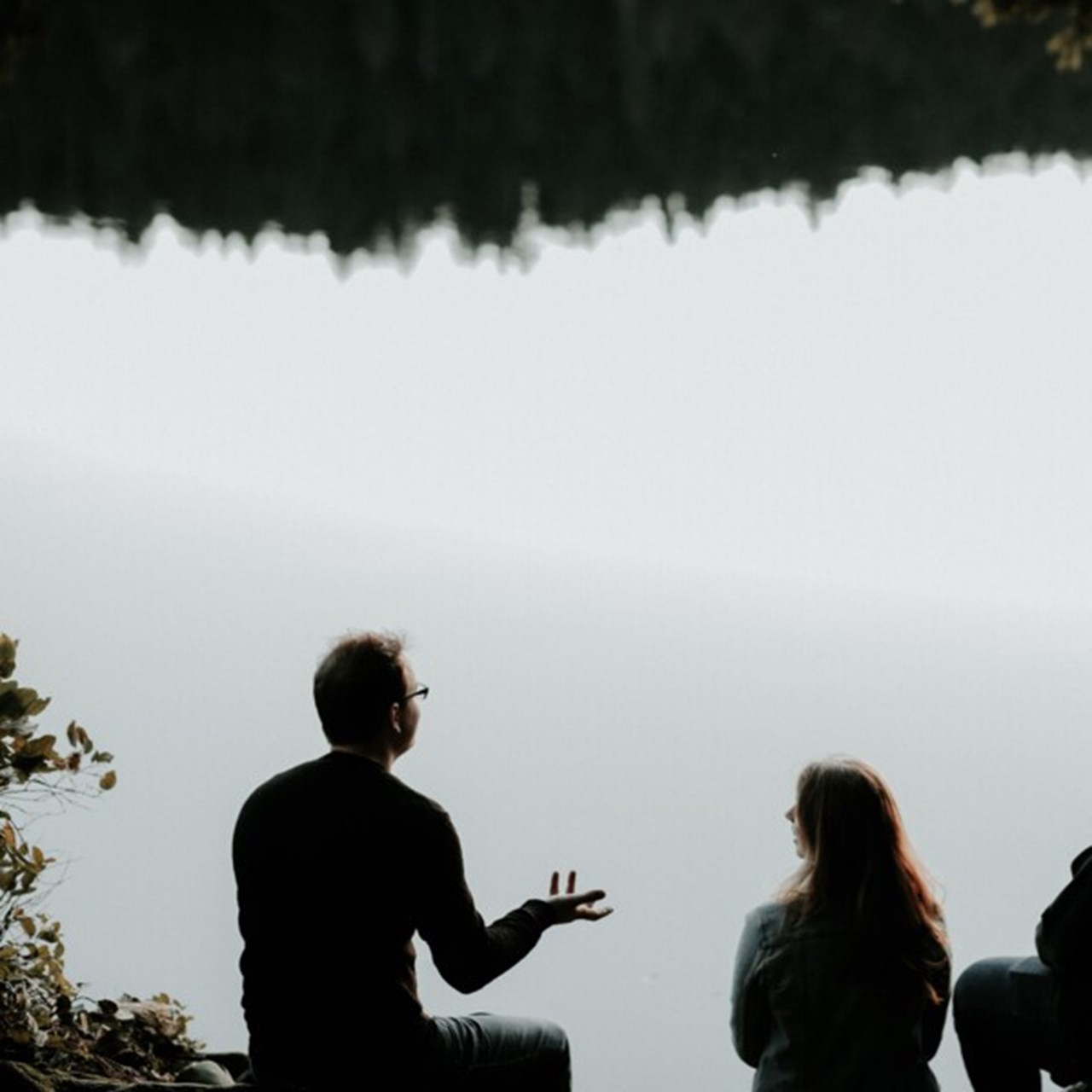 The silhouette of three people talking at a lake