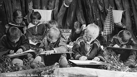Historical black and white interior photo of several Sami children attending nomadic Sámi school in Vaisaluokta, Norrbotten.