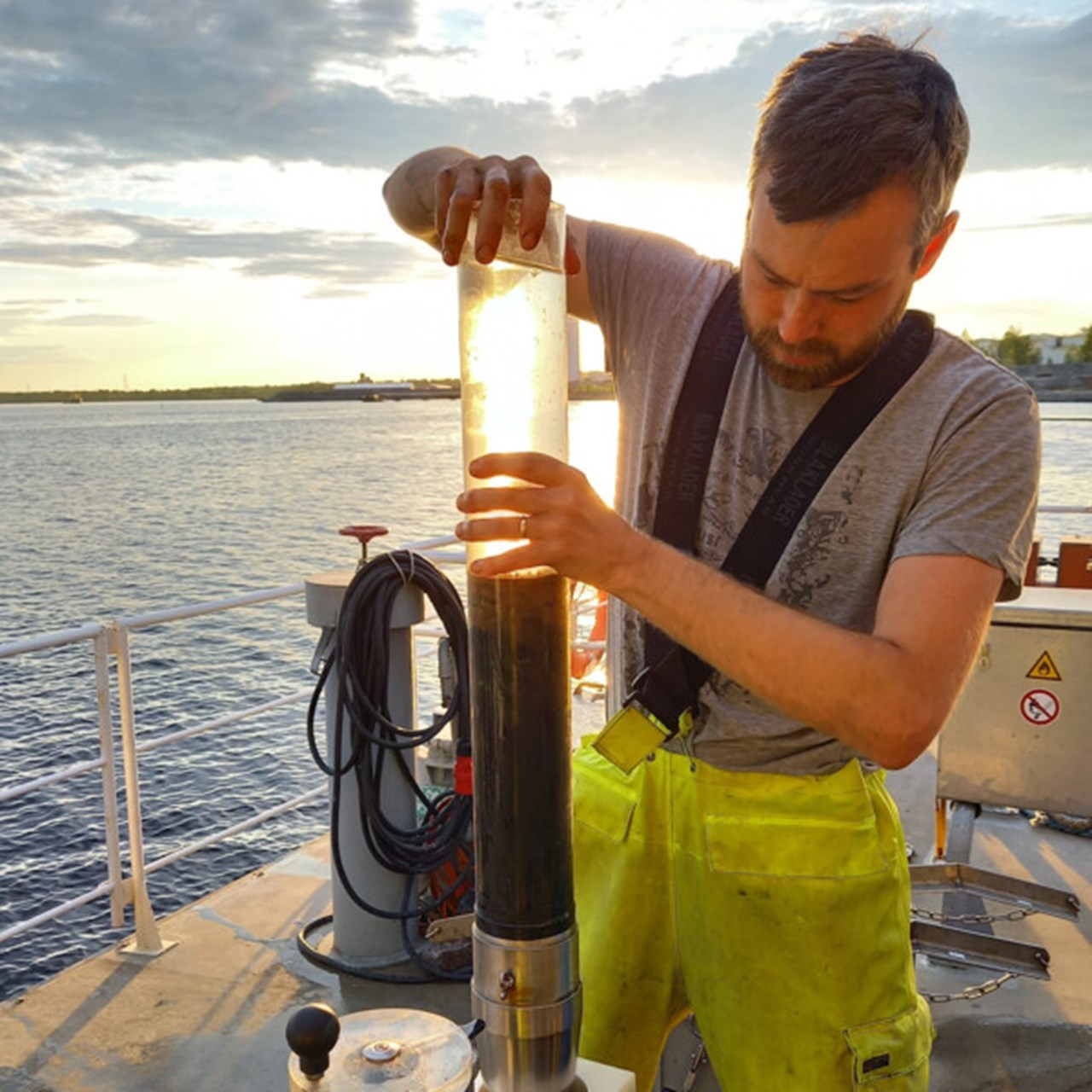 En person i gula galonbyxor håller i ett rör med sediment.