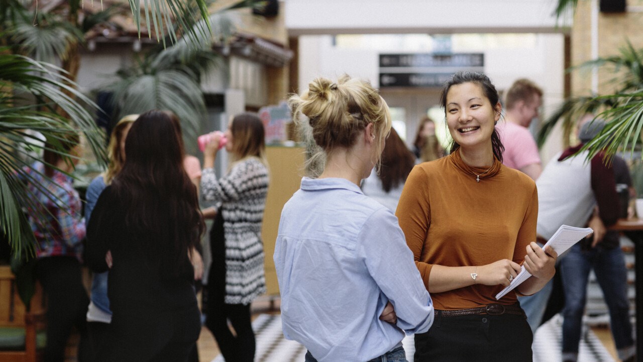 Bild på två studenter i förgrunden som samtalar i Beteendevetarhuset.