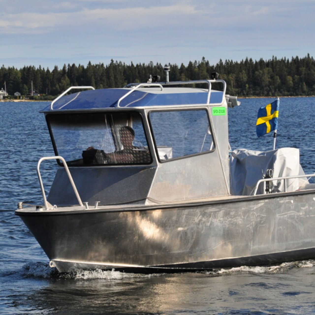 En båt av metall med stor hytt i fören och flagga i aktern