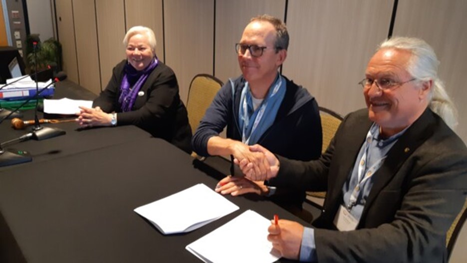 Liisa Holmberg , Keith Larson, and Lars Kullerud at a table. Keith and Lars shake hands after signing a cooperation agreement.