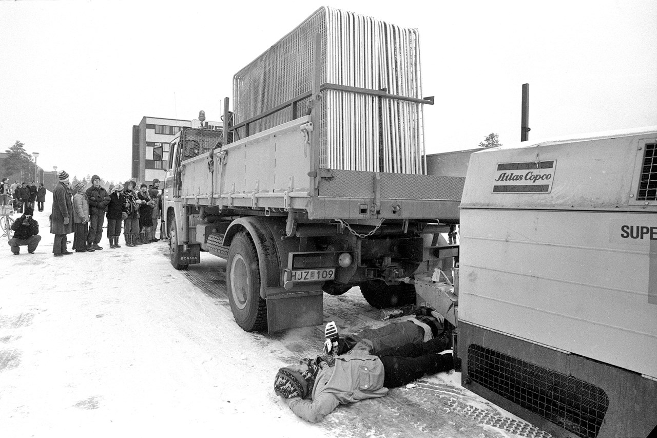 Två personer ligger på marken mellan lastbil och släpvagn