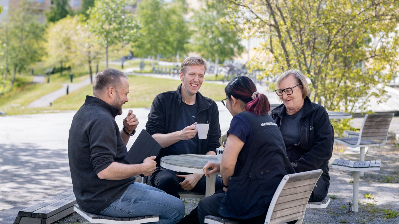 Fyra personer sitter utomhus och dricker kaffe i vårsolen.