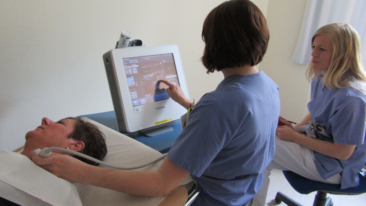 Sköterska för ultraljudsapparat över patients hals och studerar skärmen. En annan sköterska tittar på