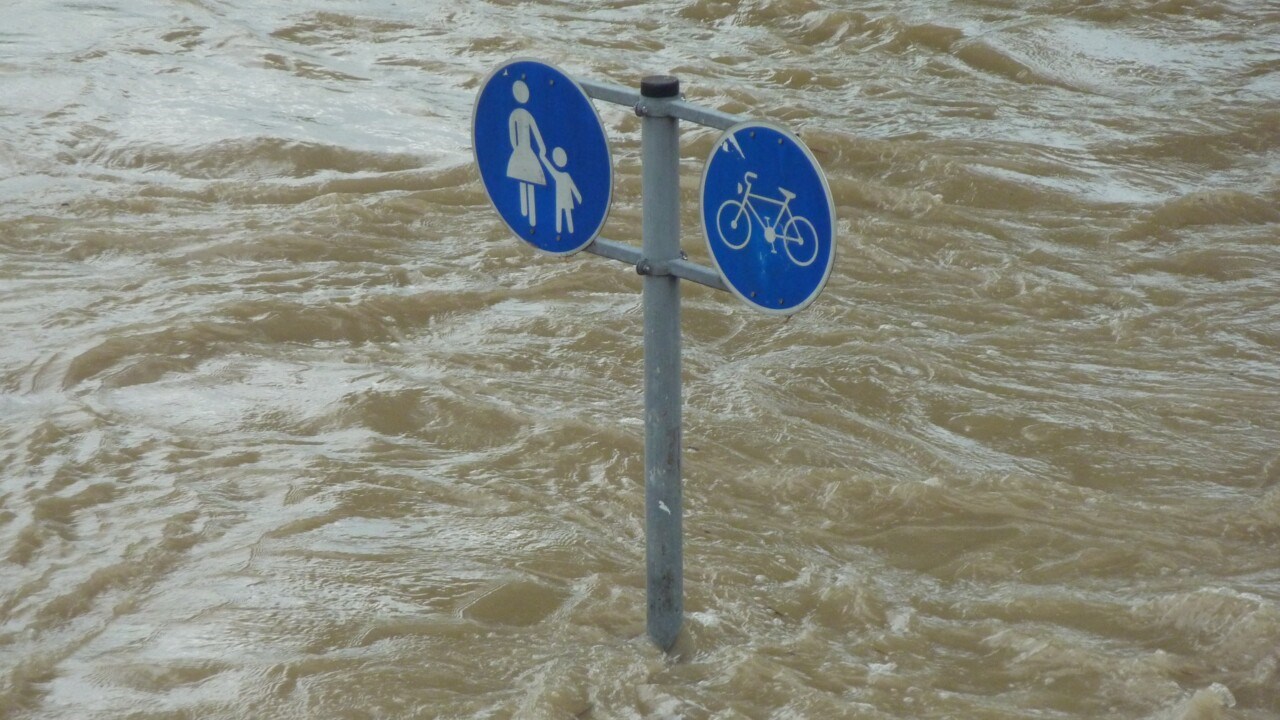 En skylt för gång- och cykelbana står mitt i vattnet på en översvämmad yta.